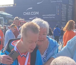 Mark in zijn blauwe jas samen mijn zijn moeder met wit haar en een blauw vest aan. 